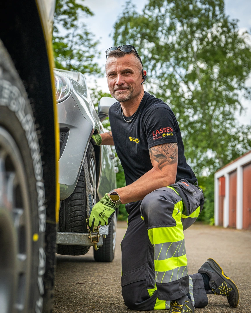 Mechaniker kniet beim Reifenwechsel neben einem Auto