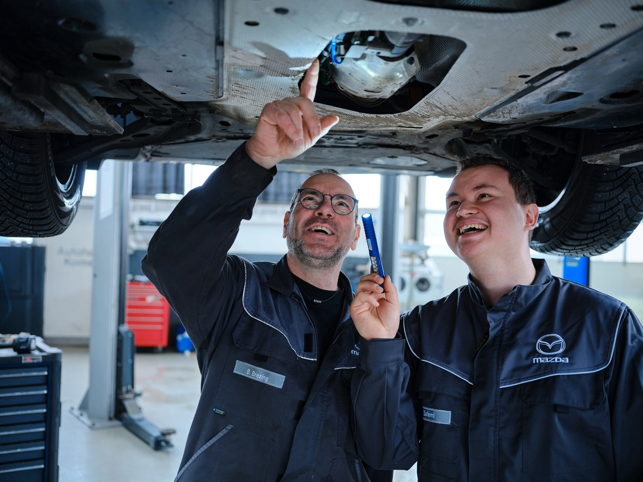Zwei Mechaniker schauen gemeinsam unter ein Auto auf der Hebebühne