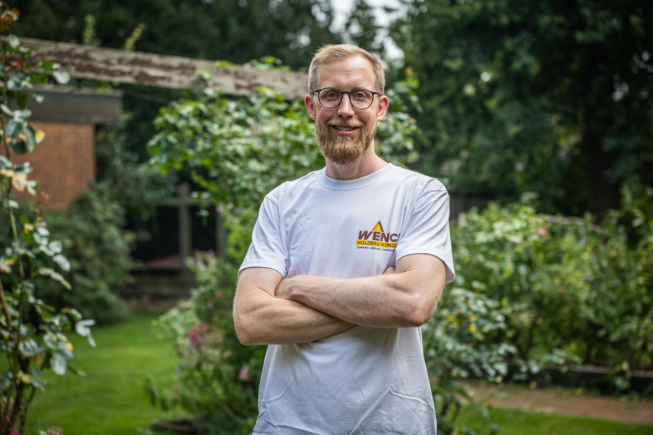 Ein Mann steht mit verschränkten Armen im Garten