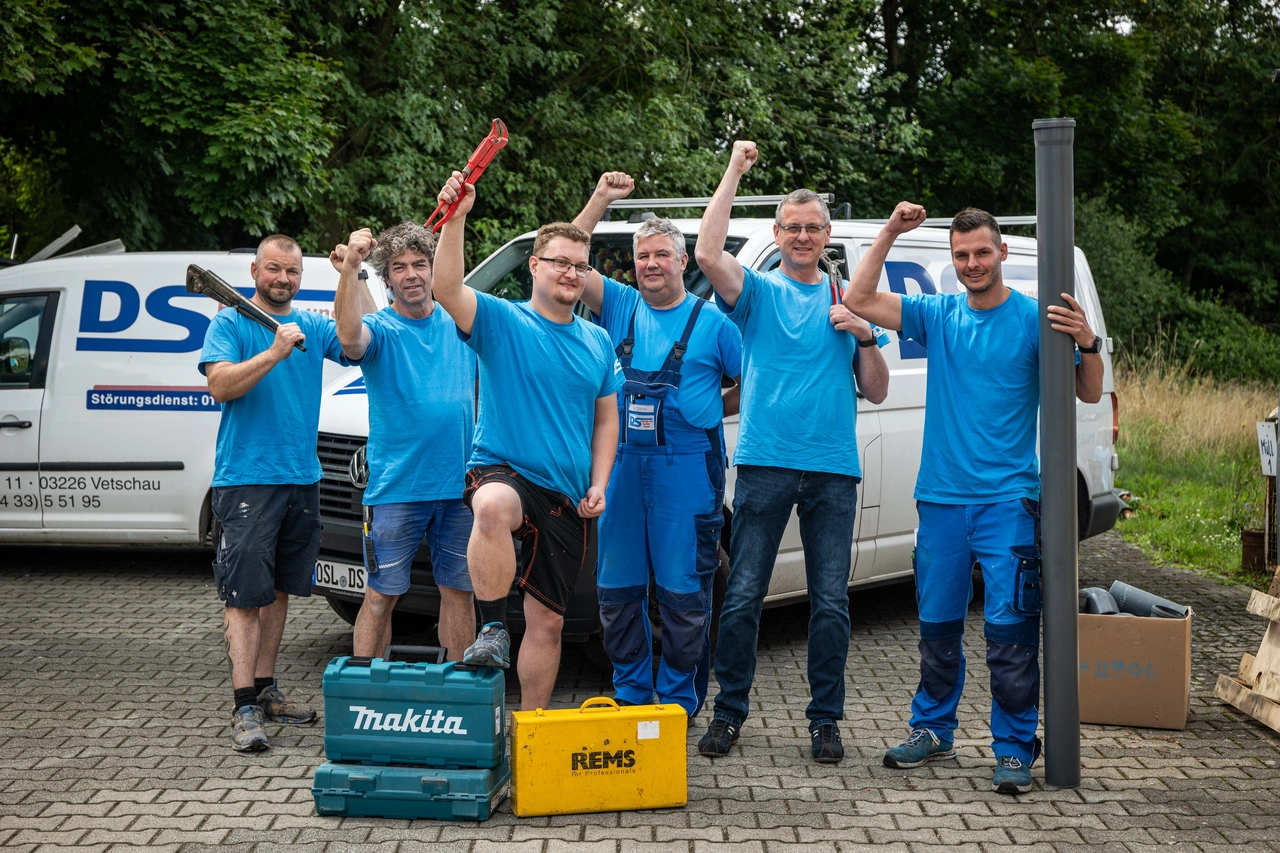 Ein Team in blauer Arbeitskleidung jubelt vor den Firmenwagen