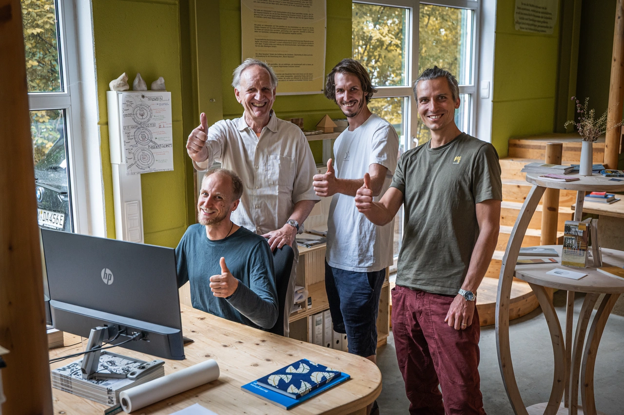 Vier Kollegen um einen Tisch mit Laptop, alle zeigen den Daumen nach oben