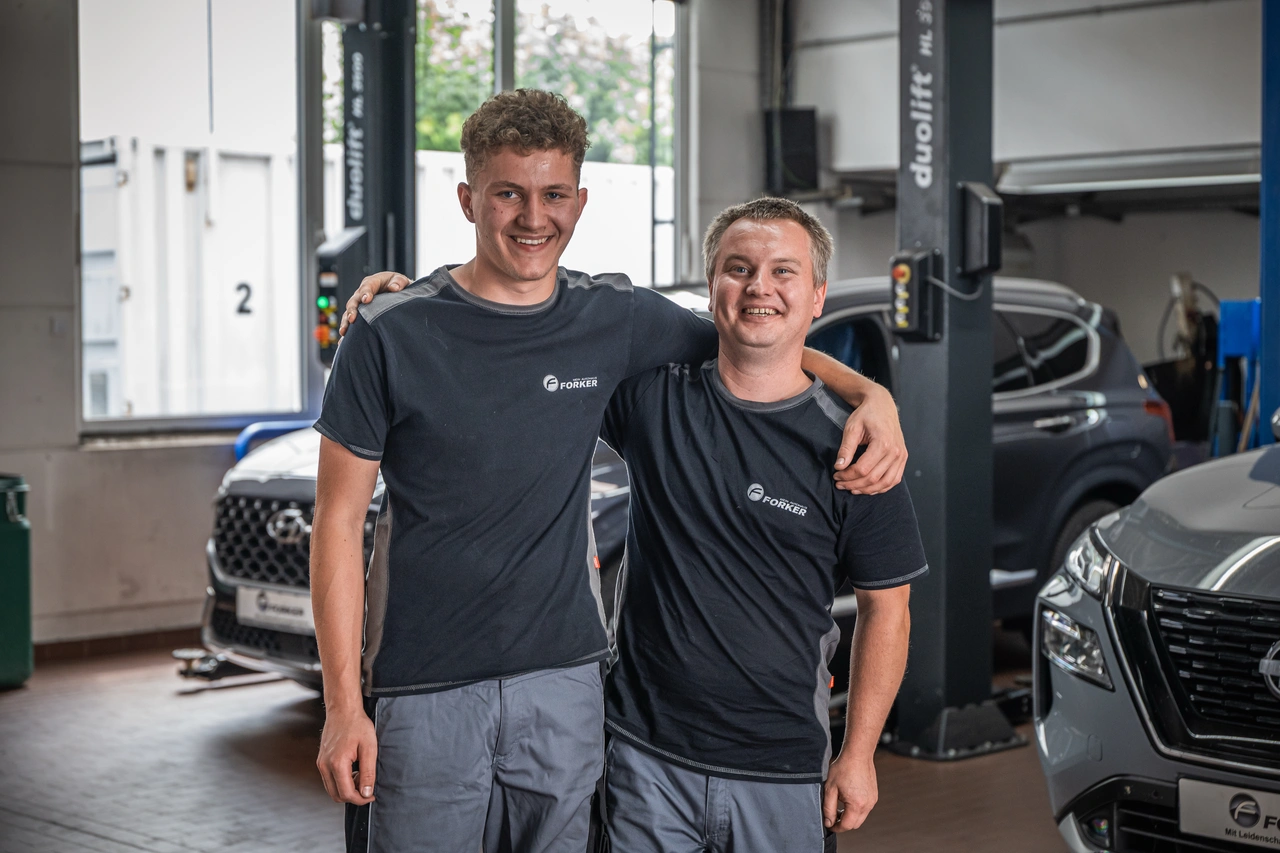 Zwei junge Kollegen in der Werkstatt, einer legt dem anderen den Arm um die Schulter