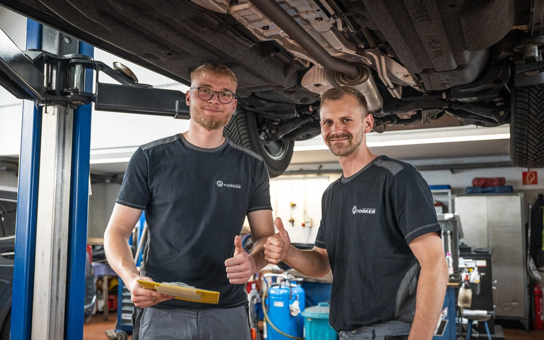 Zwei Mechatroniker unter einem Fahrzeug in der Autohauswerkstatt