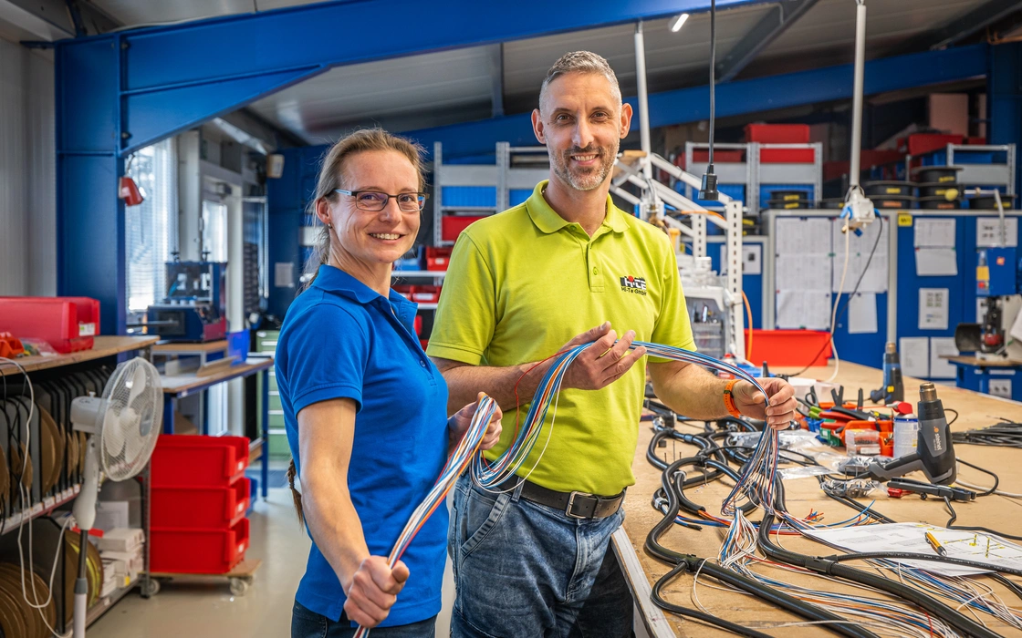 Zwei Mitarbeiter mit Kabelbäumen an der Werkbank einer Fertigung