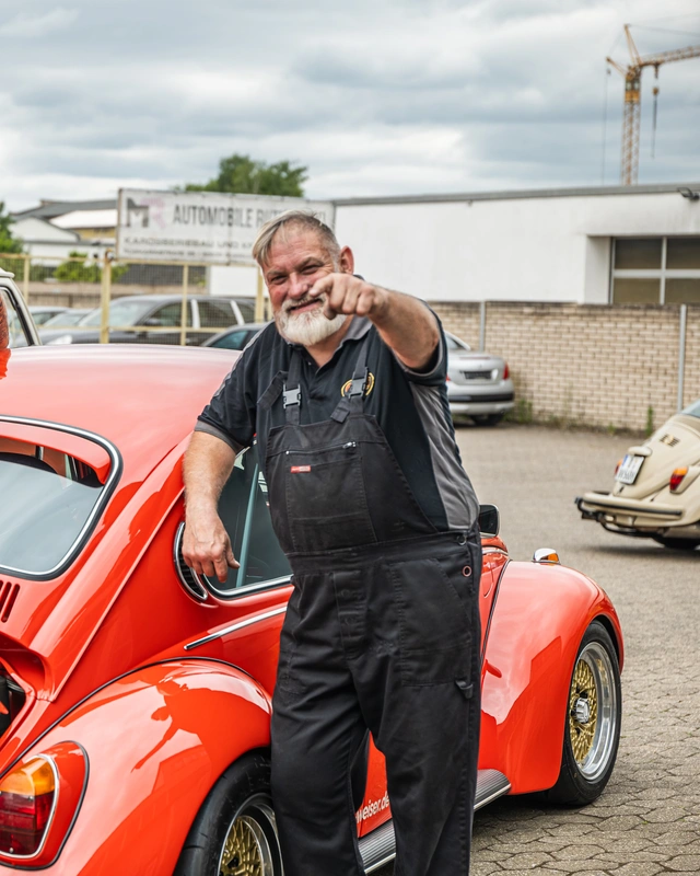 Kfz-Meister mit Latzhose vor einem restaurierten Oldtimer