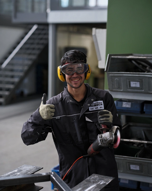 Metallbauer mit Schutzbrille und Winkelschleifer in der Werkstatt