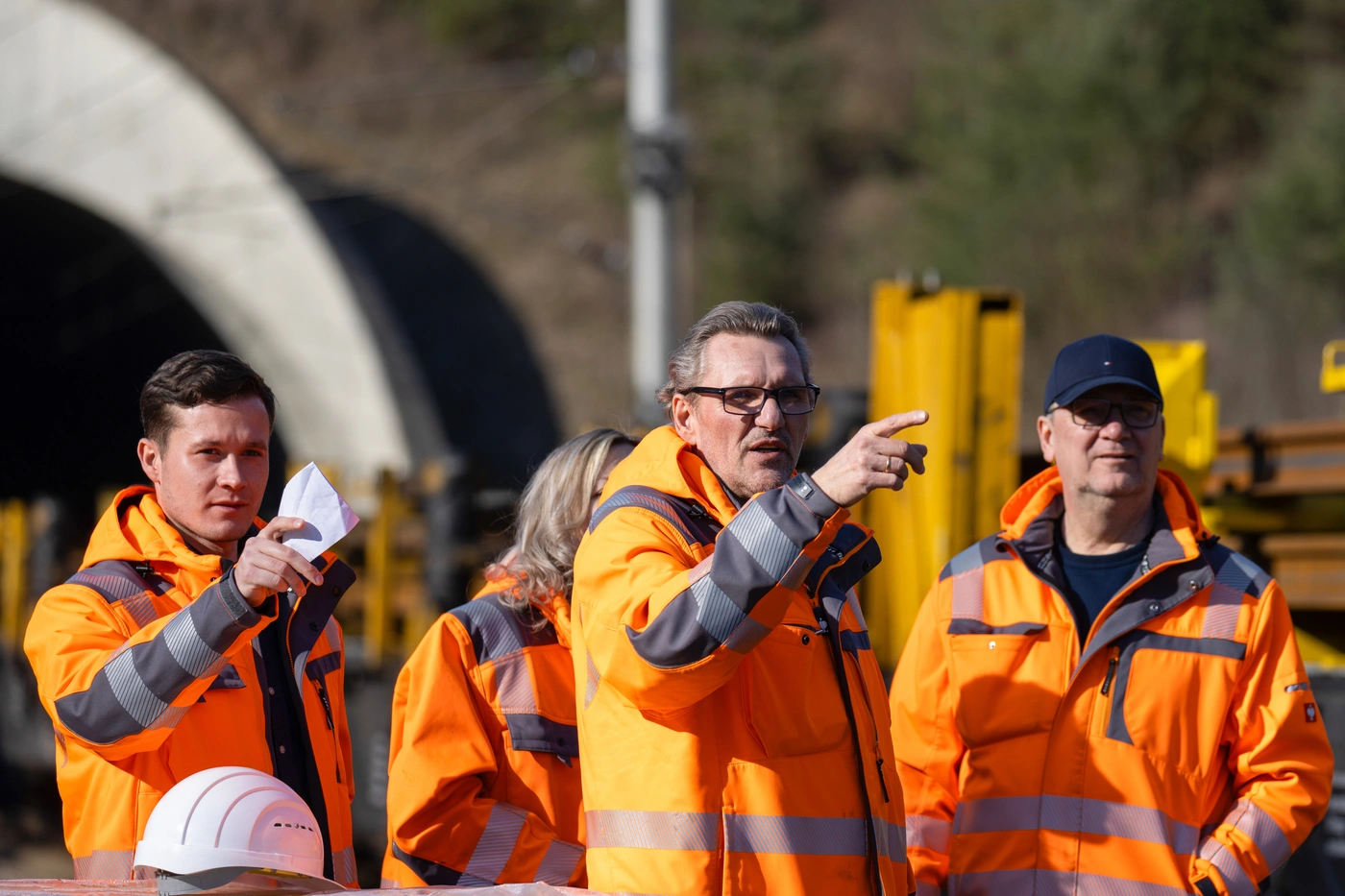 Bauleute in orangefarbener Warnkleidung besprechen sich vor einem Tunnelportal