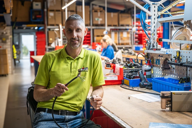 Mitarbeiter in der Fertigung an einer Montagelinie, im Hintergrund Materialkisten und Werkbänke