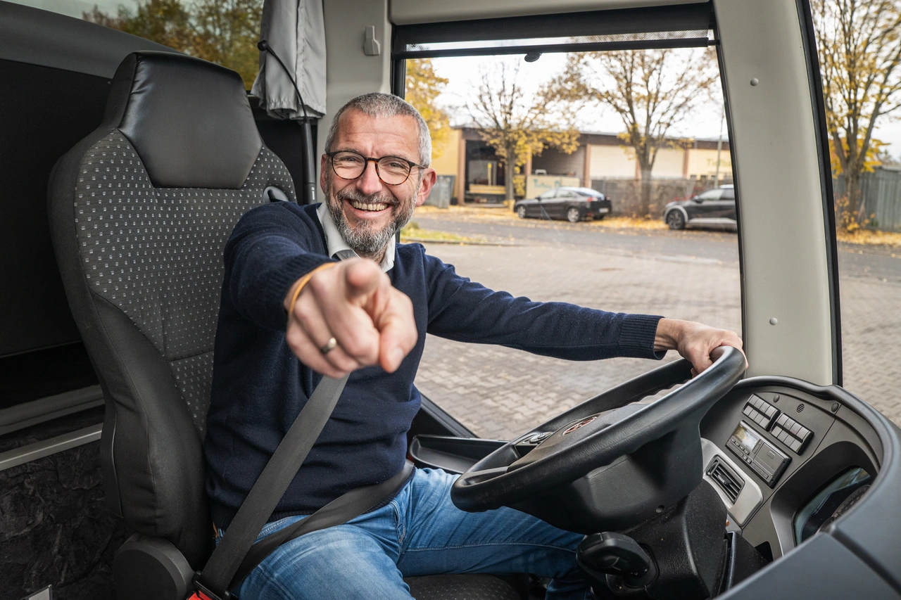 Ein Mann am Steuer eines Busses zeigt in die Kamera