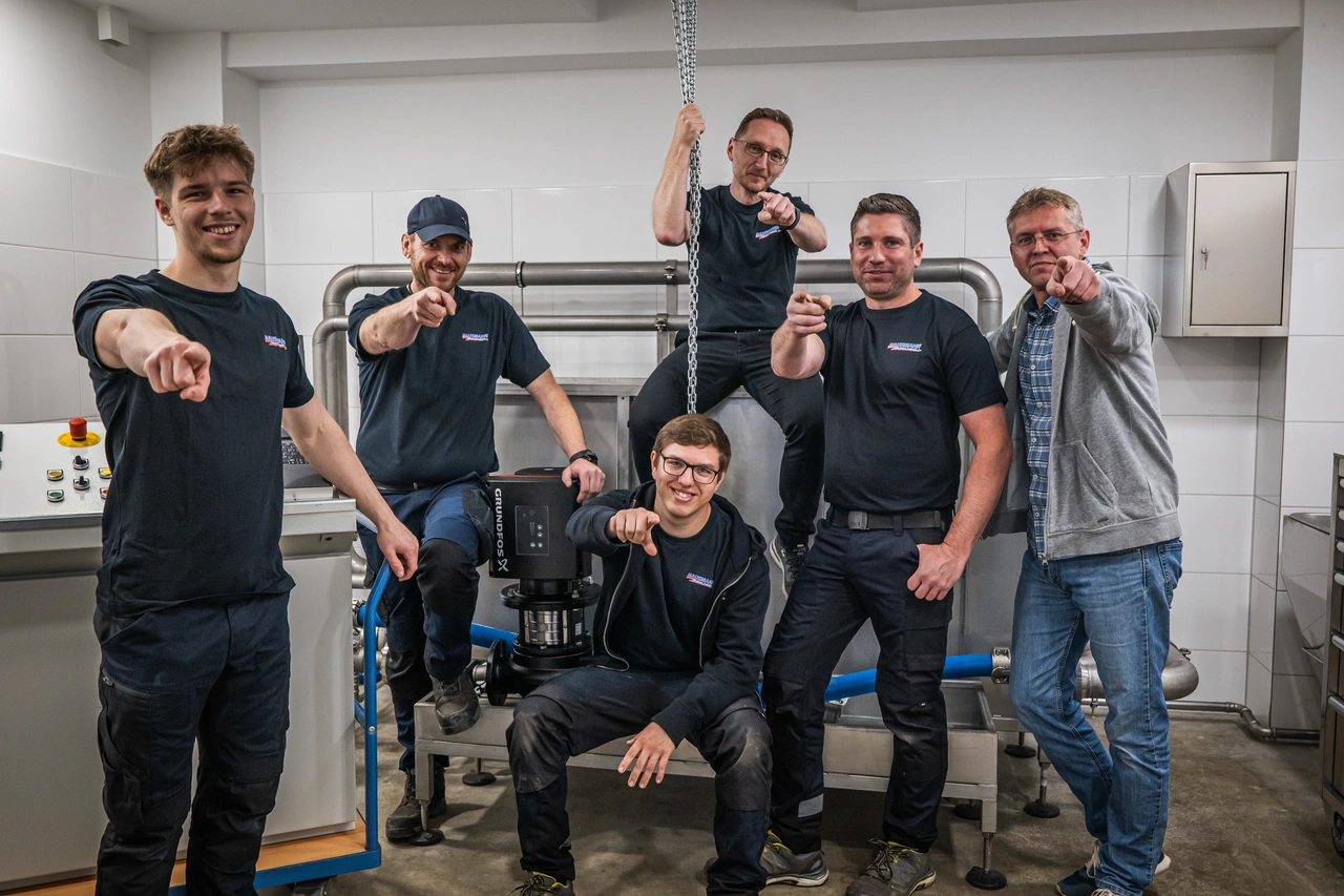 Ein Team in der Werkstatt, alle zeigen in die Kamera