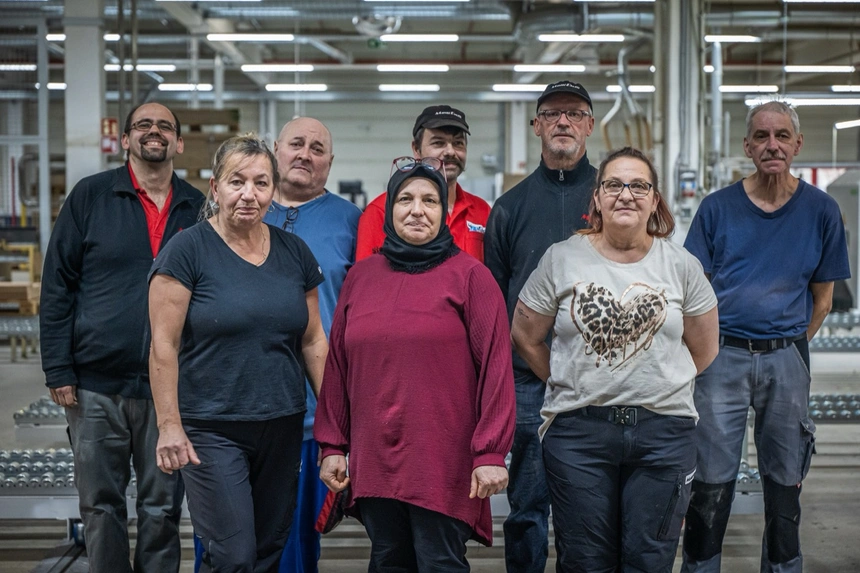 Maschinenführer prüft an einer Produktionsanlage ein gefertigtes Bauteil, im Hintergrund läuft die Fertigungsstraße