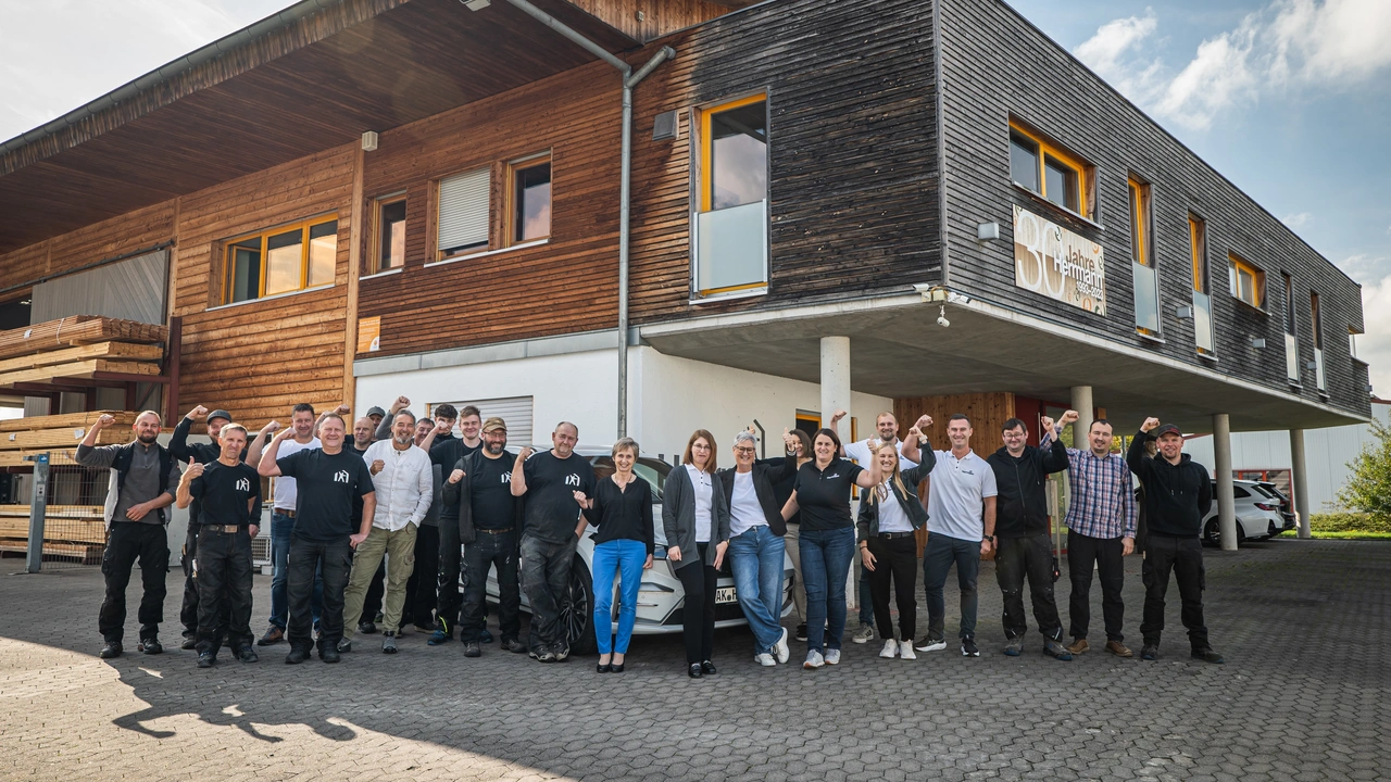 Die ganze Belegschaft eines Holzbaubetriebs jubelt vor dem Firmengebäude mit Holzfassade