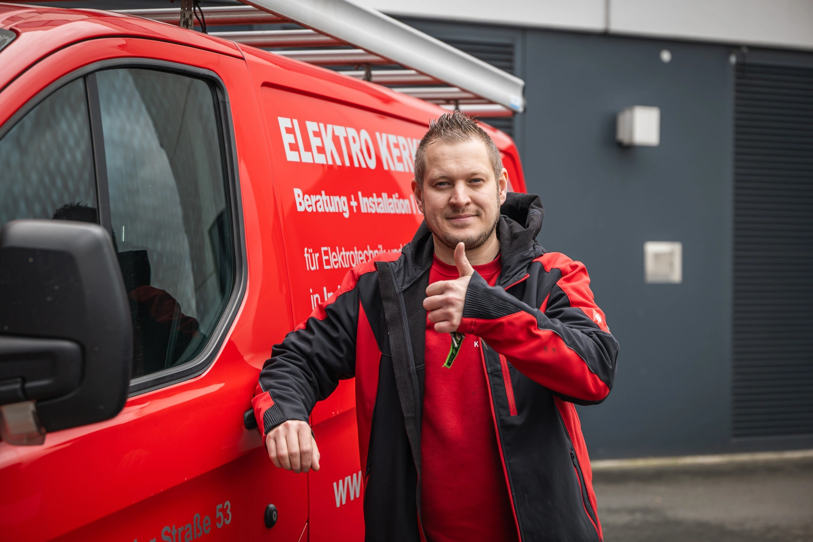 Elektromeister vor dem roten Firmenwagen